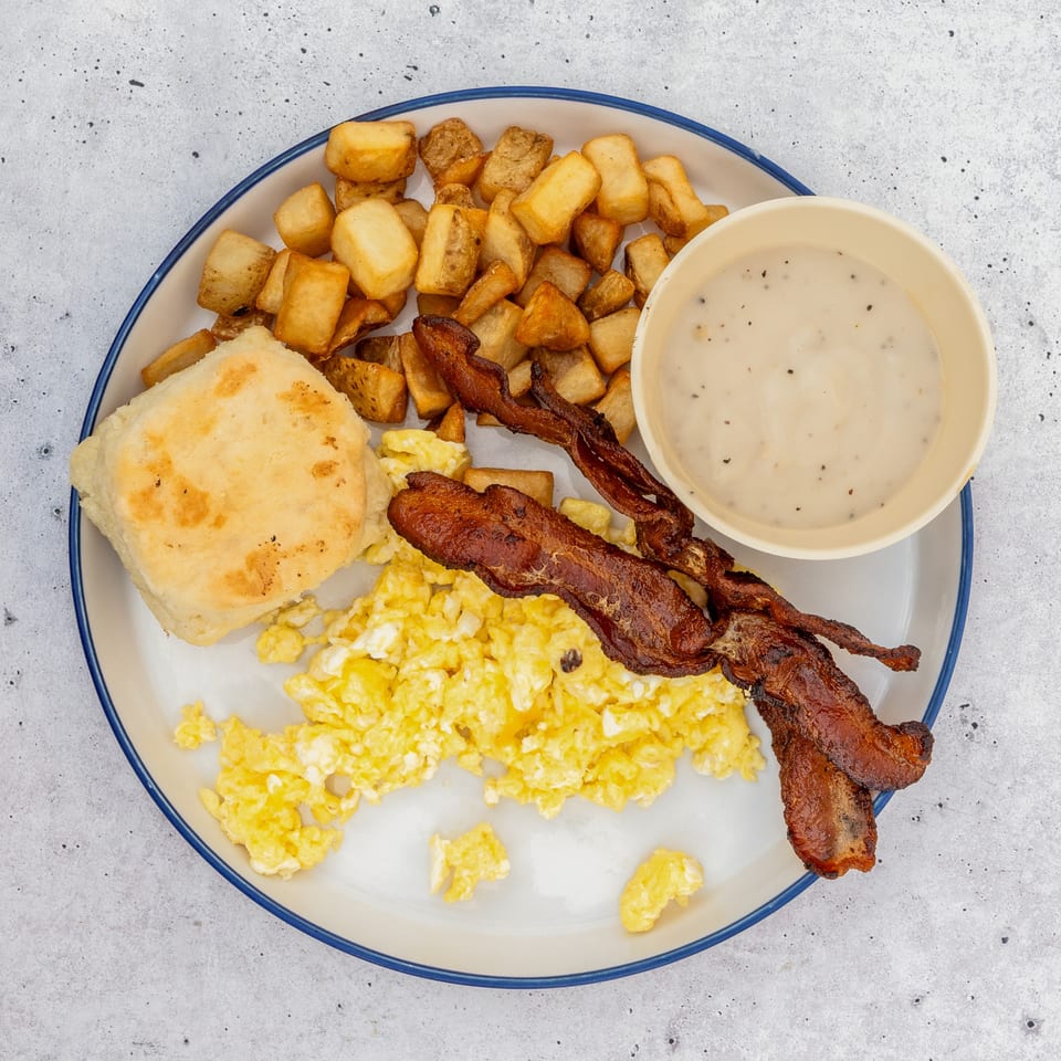 Corner Stone Café breakfast plate with scrambled eggs, crispy bacon, home fries, biscuit, and gravy.