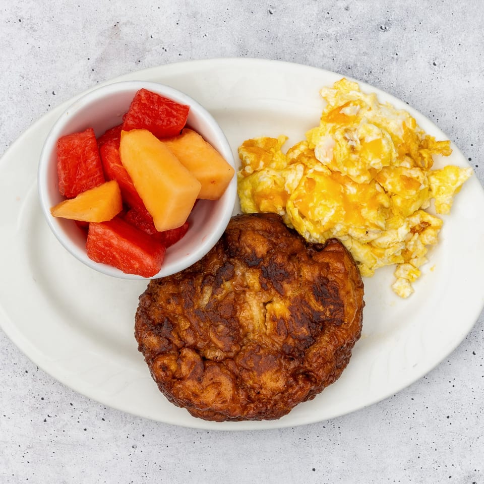 A breakfast plate with scrambled eggs, a crispy hash brown patty, and a side of fresh fruit.